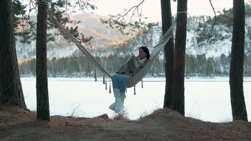 Woman Relaxing in Hammock By Frozen Lake in Winter Forest