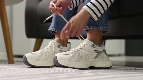 Woman tying shoelace of white sneaker indoors, closeup
