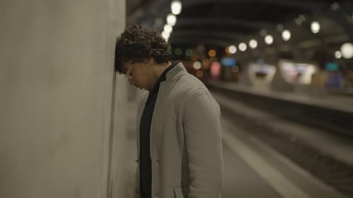 Young Man With Black Curly Hair Waiting Lonely at Train Station at Night
