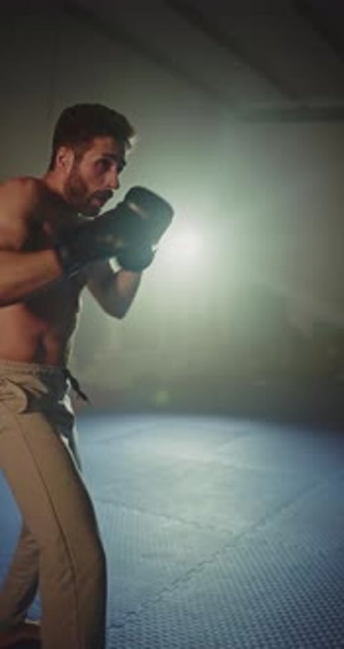 Muscular Man Boxing Heavy Bag in Dark Gym