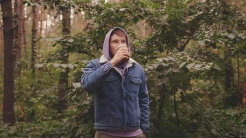 Young Man in Warm Clothes Drinking Coffee From Paper Cup Standing in Forest