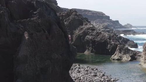 Young Woman Stands with Outstretched Arms on Volcanic Rock Overlooking Atlantic Ocean at La Palma