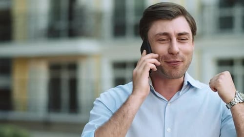 Successful businessman celebrating victory on city street talking on mobile phone