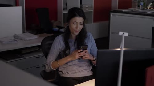 Woman Using Phone in Office at Night