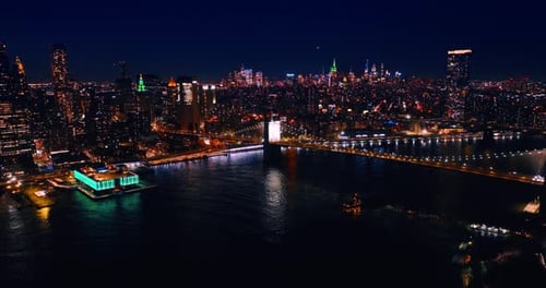 Drone footage over the East River approaching the Manhattan Bridge at night.