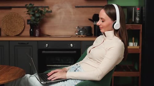 Woman Typing on Laptop with Headphones in Kitchen