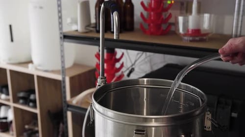 Água entrando e enchendo uma panela de metal em uma instalação caseira de fabricação de cerveja, de perto