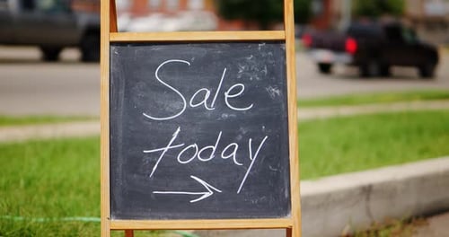 Sale today chalkboard and wood A-frame sign outside next to green grass and road with cars driving b