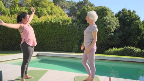 Mujeres mayores calentándose en colchonetas con botellas de agua, estirándose, dándose un paso, saludando, abrazándose junto a la piscina