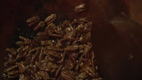 Close up slow motion shot of roasted caramelised pecan nuts being stirred with a big wooden paddle.
