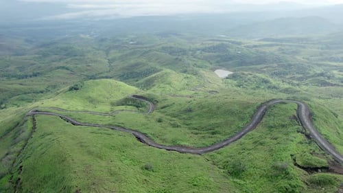 Drone footage of a winding mountain road cutting through lush green hills