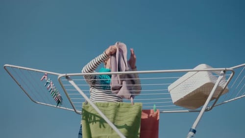 A Middleaged Woman Hangs Laundry on a Drying Rack in a Backyard She Wears a Striped Shirt and a Blue