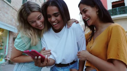 Young Happy Female Friends Having Fun Using Mobile Phone at City Street