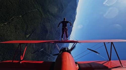 Wing Walker Standing on Biplane Over Mountains