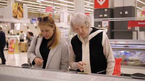 An Adult Woman Helps a Grandmother to Buy Frozen Vegetables in a Hypermarket