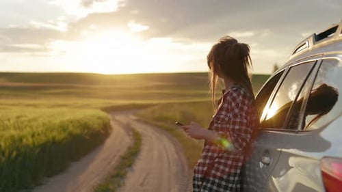 Woman Using Phone Beside Car at Sunset