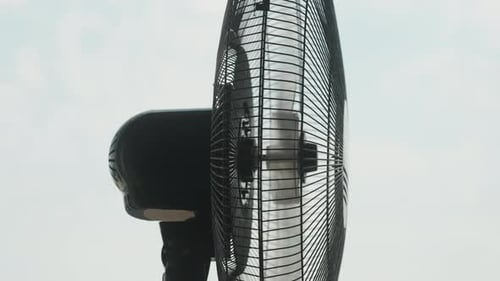 Schwarzer Bodenventilator dreht sich, Seitenansicht gegen Himmel und Wolken, Nahaufnahme.