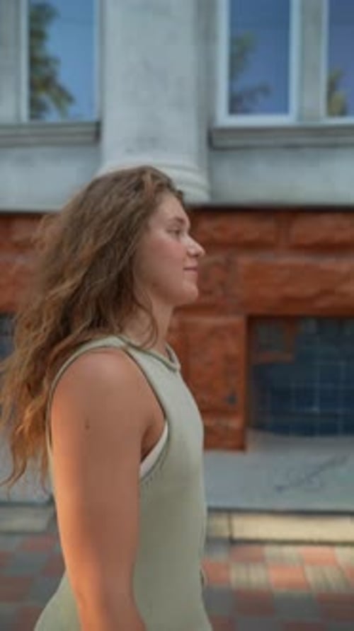 The Radiant Evening Sun Illuminates a Girl's Red Curly Hair As She Walks Through the City