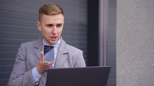Man Talks on Phone with Laptop Outdoors
