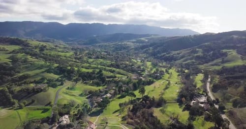 Country side lush green mountains, covered with trees, under a blue sky with clouds