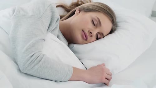 A charming young woman is sleeping in the white bed at home