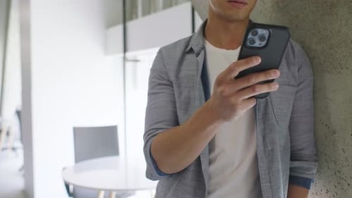 Businessman texts on smart phone in modern office building slow motion pan up