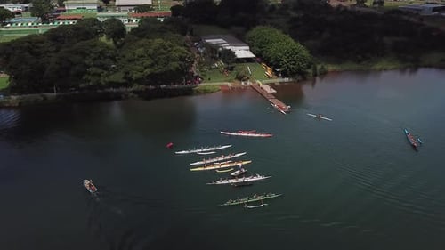 Aerial descending view towards colourful group of long athletes row boats on lake water