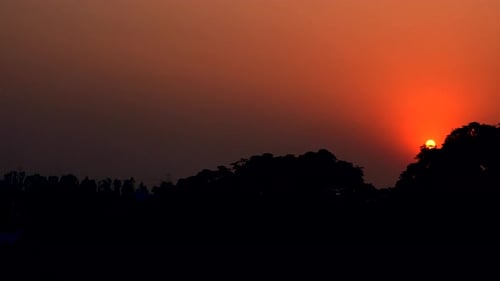 Le soleil brille dans le ciel orange foncé derrière le sommet de la montagne