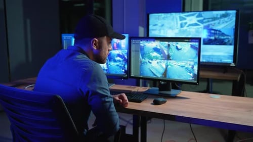 Security Guard Works on a Computer with Surveillance CCTV Video Footage in a Monitoring Center with