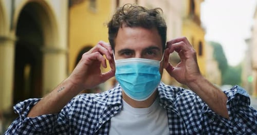 Authentic shot of young man is putting a medical mask to protect hisself from disease in city cent