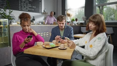 Three Multiracial Friends are Using Phones in a Cafe
