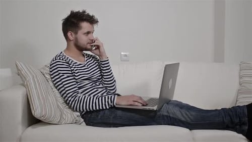 Young man with laptop working on couch in modern living room studio shot