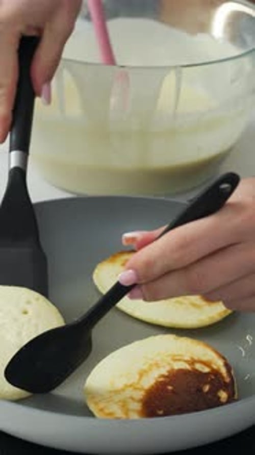 Vertikal von Hand, wie Pfannkuchen mit einem Spatel in einer Pfanne umgedreht werden. Nahaufnahme