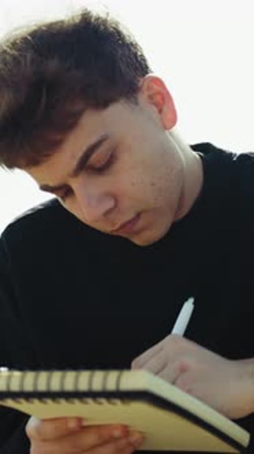 Man Writing Ideas On A Notebook With A Pen On A Park Bench