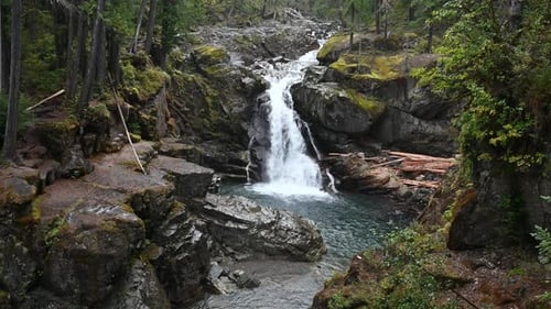 Aerial drone view of a mountain stream cascading into a waterfall surrounded by rocky terrain and fo