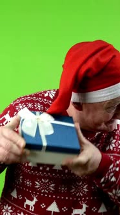 Senior Man in Santa Hat and Xmas Sweater Opening Gift Box and is Delighted