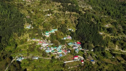 Aerial drone shot of a hidden village in the mountains, surrounded by vast meadows and forests.