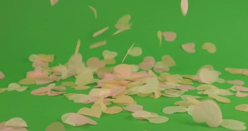 Falling heart-shaped confetti on a green background.