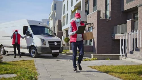 Caucasian Delivery Man in Face Mask and Gloves Handling Parcel Box Walking Along the Street with