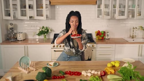 Woman Eating Tomatoes in Bright Kitchen