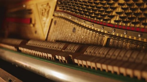 Close-up of piano hammers striking strings inside an upright piano with warm cinematic lighting