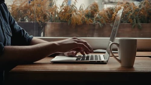 Young male freelancer chatting on mobile phone while sitting front open laptop computer cafe