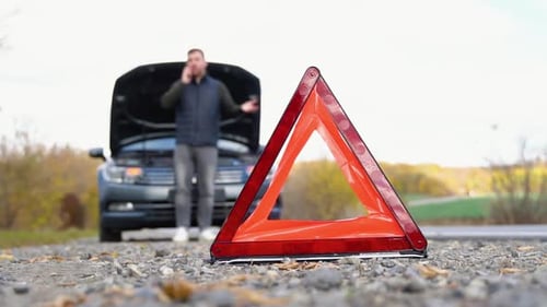 Road Side Warning Triangle Warning Oncoming Traffic of a Broken Down Car with a Man Using His Cell