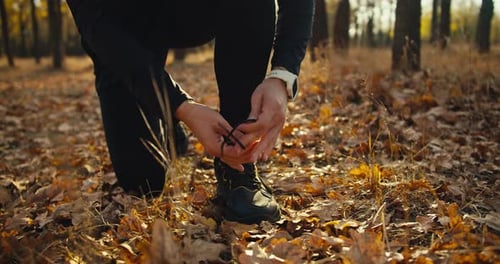 Close Up a Man in a Black Sports Uniform Ties the Laces on His Sneakers Before Starting His Race