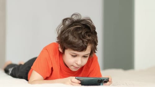 Boy Using Mobile Phone While Lying on Bed