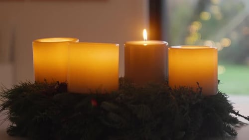 Three glowing candles on evergreen wreath, festive ambiance.