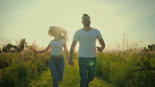 Couple Runs Hand-in-Hand Through Grassy Field