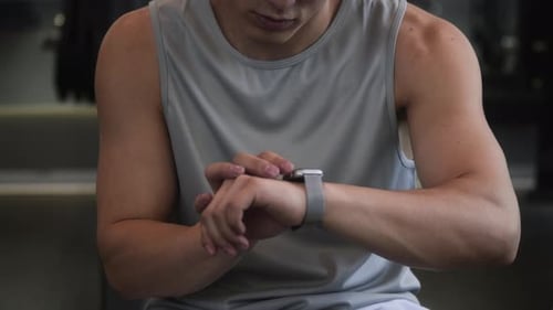 Unbekannter Mann, der während des Trainings im Fitnessstudio den Timer auf der Smartwatch einstellt
