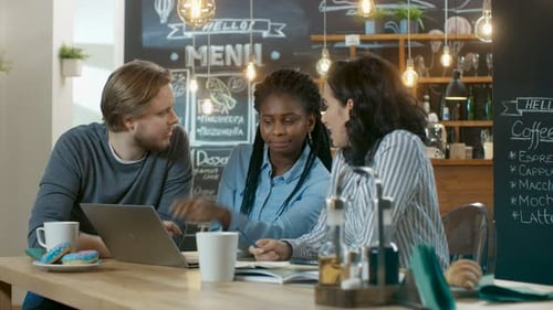 Three Young People in the Coffee Shop, They Work on a Laptop and Talk. In the Background Stylish Ca