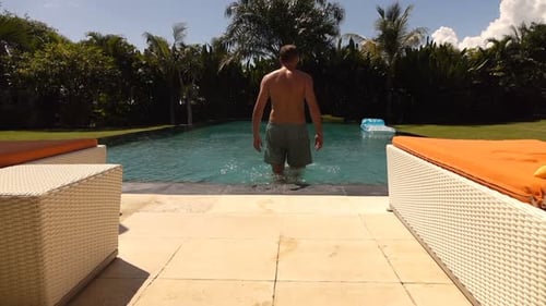 Young man walking into swimming pool and enjoying sunny summer vacation in slow motion
